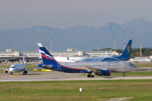 Aeroflot Airbus A320-214 airplane maneuvering on the Malpensa airport runway. In the background the buildings of Terminal 1 and parked airplanes. - MyVideoimage.com