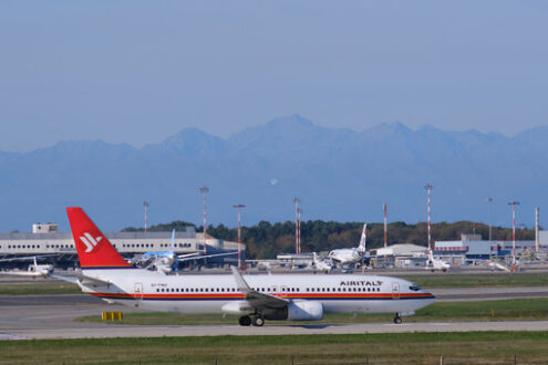 Air Italy Boeing 737-800  airplane on the Malpensa airport runway. In the background the buildings of  Cargo Terminal and parked airplanes. - MyVideoimage.com