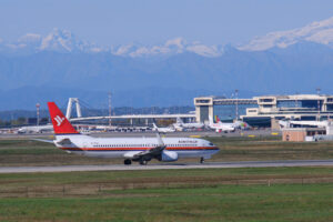 Air Italy Boeing 737-800  airplane on the Malpensa airport runway. In the background the buildings of   Terminal 1 and parked airplanes. - MyVideoimage.com