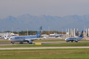 Air Italy jet airplane on the Malpensa airport runway. In the background the buildings of Terminal Cargo and parked airplanes. - MyVideoimage.com