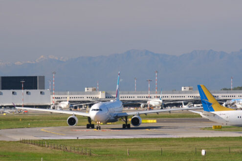 Air Italy jet airplane on the Malpensa airport runway. In the background the buildings of Terminal Cargo and parked airplanes. - MyVideoimage.com