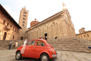 Antique red Fiat 500 car parked in the square of Massa Marittima. The car awaits the bride and groom at the cathedral wedding. Foto automobili. Cars photos.