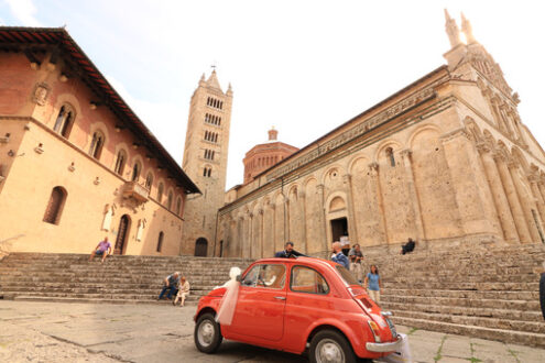 Antique red Fiat 500 car parked in the square of Massa Marittima. The car awaits the bride and groom at the cathedral wedding. Foto automobili. Cars photos.