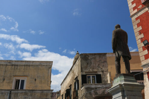 Antonio Scialoja. Bronze monument to Antonio Scialoja in a square in Procida. In the background the façades of the Mediterranean houses. - MyVideoimage.com | Foto stock & Video footage