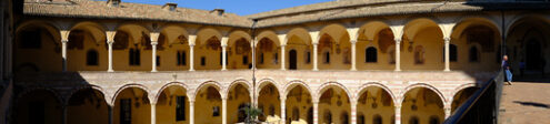 Assisi cloister with columns. Cloister with columns and arches at the Basilica of San Francesco in Assisi. In the center of the courtyard there is a well in beige stone. - MyVideoimage.com | Foto stock & Video footage