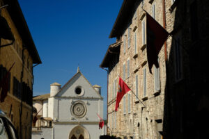 Assisi road with flags. Historic Via San Francesco in Assisi leading to the famous basilica. Flags fly on the facades of the stone and brick houses. - MyVideoimage.com | Foto stock & Video footage