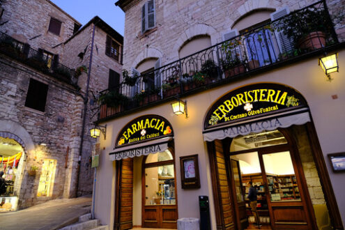 Assisi square. Municipality of Assisi square with old pharmacy and bar area. Illuminated signs in the city of San Francesco with the lights of the night. - MyVideoimage.com | Foto stock & Video footage