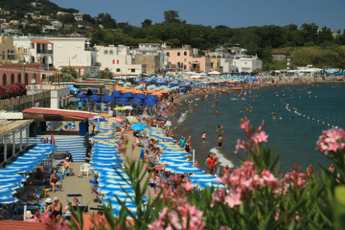 Beach with umbrellas, sunbeds and deck chairs. Bathing establishments and houses in the town of Ischia. - MyVideoimage.com