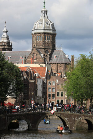 Bridge on a city canal with people walking. In the background an ancient church with a dome and bell tower. - MyVideoimage.com