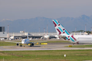 Bulgaria Air Airbus A320-214 airplane on the Malpensa airport runway. In the background the buildings of Terminal 1 and parked airplanes. - MyVideoimage.com