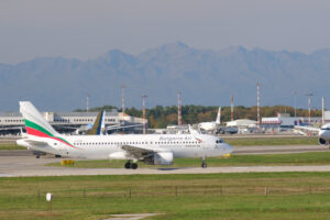 Bulgaria Air Airbus A320-214 airplane on the Malpensa airport runway. In the background the buildings of Terminal 1 and parked airplanes. - MyVideoimage.com