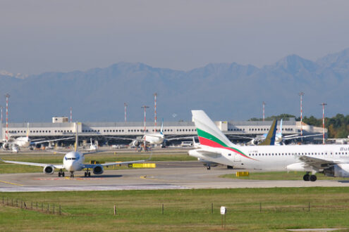 Bulgaria Air Embraer 190/195 airplane on the Malpensa airport runway. In the background the buildings of Terminal 1 and parked airplanes. - MyVideoimage.com