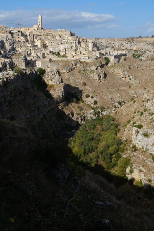 Case a Matera. Panorama of houses and of the Sassi of Matera with roofs and streets. Blue sky with church and bell tower with blue sky background with clouds. - MyVideoimage.com | Foto stock & Video footage