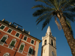 Chiesa Lerici La Spezia. Palace and bell tower of the church of Lerici with a blue sky background and a palm tree in the foreground. - MyVideoimage.com | Foto stock & Video footage