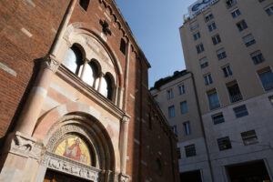 Chiesa san Babila a Milano. Brick facade of the church of San Babila in Milan. On the facade a mosaic. In the background modern buildings. - MyVideoimage.com | Foto stock & Video footage