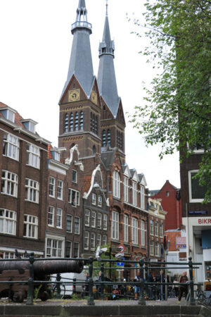 Church towers in the center of Amsterdam. In the foreground, a bridge over a canal with an old cannon. - MyVideoimage.com