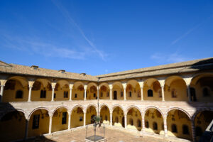 Cloister with columns and arches at the Basilica of San Francesco in Assisi. In the center of the courtyard there is a well in beige stone. - MyVideoimage.com