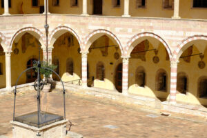 Cloister with columns and arches at the Basilica of San Francesco in Assisi. In the center of the courtyard there is a well in beige stone. - MyVideoimage.com