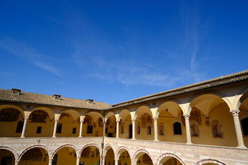 Cloister with columns and arches at the Basilica of San Francesco in Assisi. In the center of the courtyard there is a well in beige stone. - MyVideoimage.com