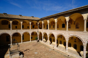 Cloister with columns and arches at the Basilica of San Francesco in Assisi. In the center of the courtyard there is a well in beige stone. - MyVideoimage.com