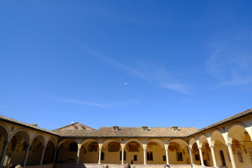 Cloister with columns and arches at the Basilica of San Francesco in Assisi. In the center of the courtyard there is a well in beige stone. - MyVideoimage.com