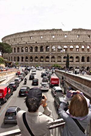 Colosseum Rome with tourists. Two tourists photograph the Colosseum. Below you see the road with car traffic and two red vans. - MyVideoimage.com | Foto stock & Video footage