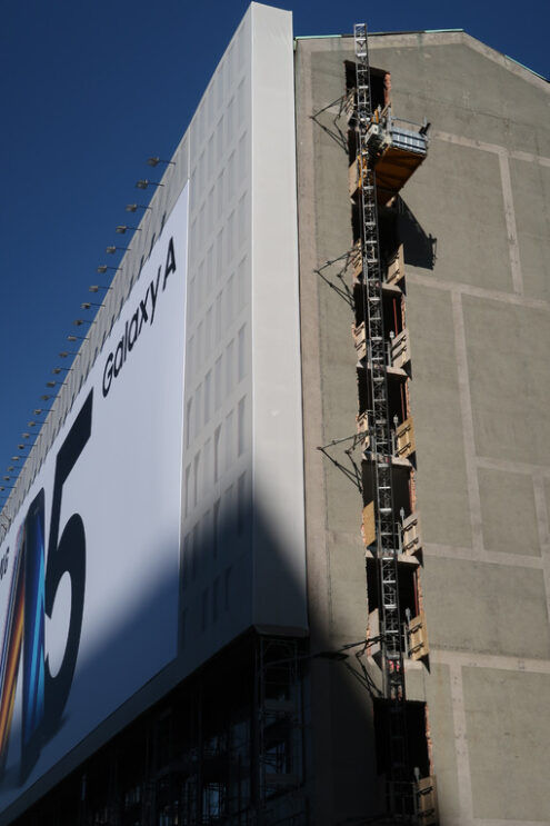 Construction site lift. Renovation of an office building in Milan. Construction site freight elevator. Advertising of a smartphone posted on the facade. - MyVideoimage.com | Foto stock & Video footage