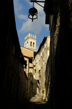 Deserted road in Assisi, Italy. Alley of the city of Assisi with bell tower and stone houses. Narrow street of the city with the walls of the stone houses. Deserted road. - MyVideoimage.com | Foto stock & Video footage