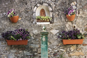 Drinking fountain with vases of purple flowers and icon with Madonna. - MyVideoimage.com | Foto stock & Video footage