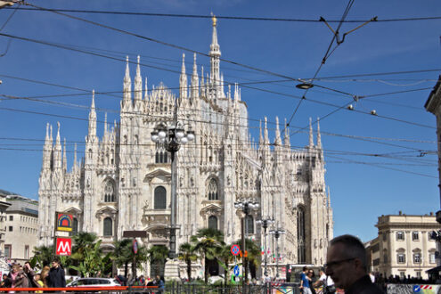 Duomo di Milano. Milan Cathedral facade with flags on blue sky. The facade of the cathedral with many people walking. Flags waving on the blue sky. - MyVideoimage.com | Foto stock & Video footage