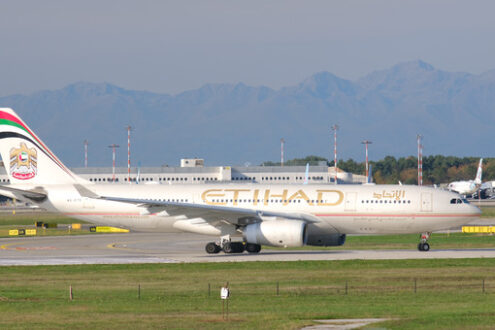 Etihad Airbus A330-243 airplane maneuvering on the Malpensa airport runway. In the background the buildings of Terminal 1 and parked airplanes. - MyVideoimage.com