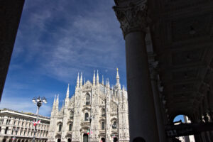 Facciata gotica Duomo di Milano. Milan Cathedral facade with  blue sky.  In the foreground the arches of the portico. - MyVideoimage.com | Foto stock & Video footage