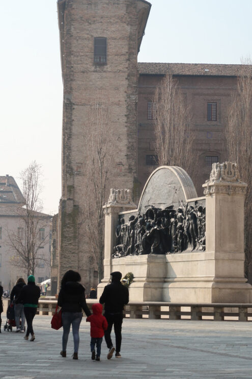 Family with child and people walking in piazza della Pace in parma. In the background the monument to Giuseppe Verdi and the Palazzo della Pilotta. - MyVideoimage.com