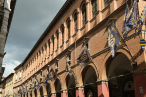 Foligno Umbria. Strada del paese. Main street of Foligno with waving flags on the facades of the houses. The ancient palaces lit by the sun with cloudy sky. - MyVideoimage.com | Foto stock & Video footage