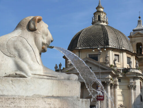 Fountain with a white marble lion statue in Piazza del Popolo in Rome. In the background the dome of one of the two twin churches. - MyVideoimage.com