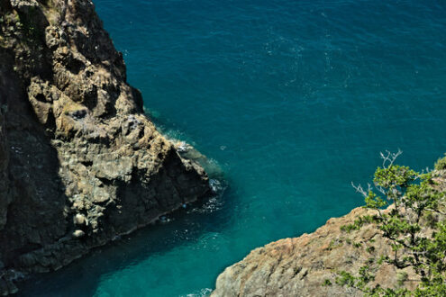 Framura near Cinqueterre. Sea waves break on the rocks of the Ligurian mountain.  Seascape with blue sea and dark red rocks. Village of Framura. - MyVideoimage.com | Foto stock & Video footage