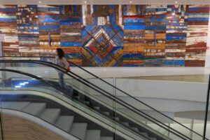 Girl on an escalator at Bari airport. Decorative panel with wooden slats made from old boats. - MyVideoimage.com