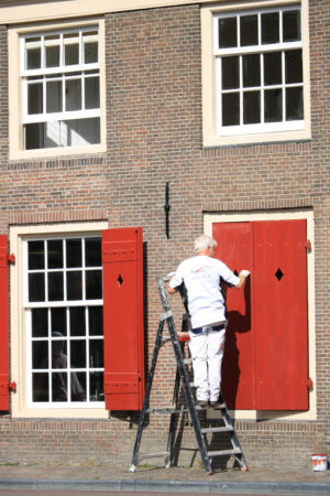 House painter paints a red shutter. Facade of a house with a bri - MyVideoimage.com