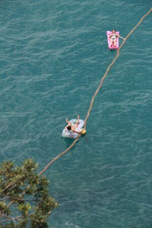 Lie down on the boat. Two people lying on a rubber boat take the sun in the middle of the sea. A rope ties them to the ground. - MyVideoimage.com | Foto stock & Video footage