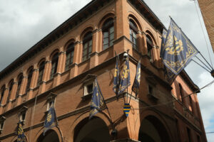 Main street of Foligno with waving flags on the facades of the houses. The ancient palaces lit by the sun with cloudy sky. - MyVideoimage.com