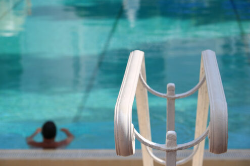 Man in the pool with green water. In the foreground, a white handrail. - MyVideoimage.com