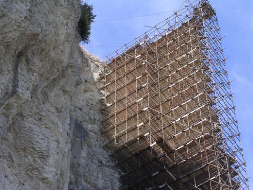 Metal scaffolding. High metal scaffolding mounted on a rock spur. Blue sky background. Cantieri edili. - MyVideoimage.com | Foto stock & Video footage