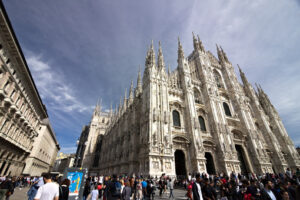 Milan Duomo. Milan Cathedral facade with flags on blue sky. The facade of the cathedral with many people walking. Flags waving on the blue sky. - MyVideoimage.com | Foto stock & Video footage