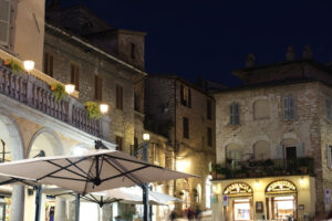 Municipality of Assisi square with old pharmacy and bar area. Illuminated signs in the city of San Francesco with the lights of the night. - MyVideoimage.com