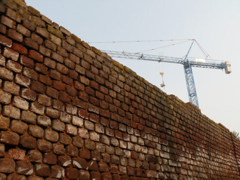 Muro di mattoni e cantiere con gru. Construction site with cranes and a solid brick wall. Cantieri edili. - MyVideoimage.com | Foto stock & Video footage