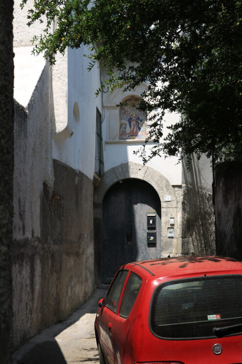 Narrow street in southern Italy with a small red car. Door with stone arched doors. Foto automobili. Cars photos.