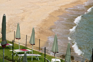 Ocher yellow beach and blue green sea. Closed umbrellas and sun loungers on green lawn. - MyVideoimage.com