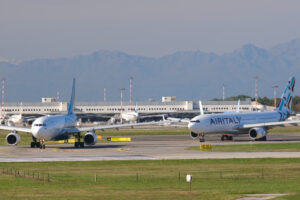 Oman Air Airbus A330-243  airplane on the Malpensa airport runway. In the background the buildings and Air Italy airplane. - MyVideoimage.com