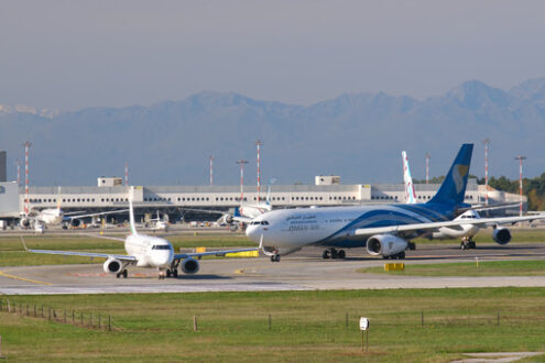 Oman Air Airbus A330-243  airplane on the Malpensa airport runway. In the background the buildings and Bulgaria Air Embraer 190/195 airplane. - MyVideoimage.com