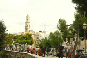 People walking in a street of the city of Bari. In the background the church bell tower. Foto Bari photo.